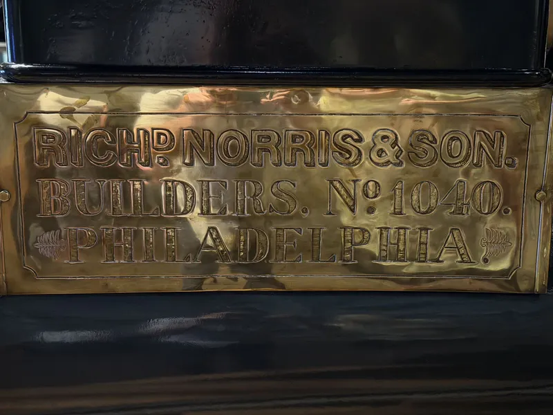 The brass builder's plate up close: "Rich'd Norris & Son, Builders, No. 1040, Philadelphia," flanked by little engraved ferns. Construction number 1040 is the serial that lets historians trace this engine through the Norris order books.