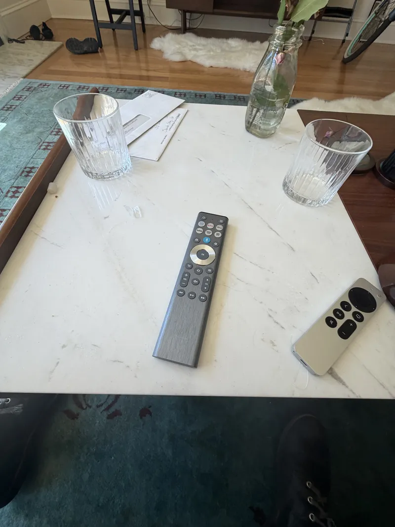 Where every field day starts: a marble coffee table, two water glasses, a milk-bottle vase, and two remotes — one universal, one Apple TV — abandoned mid-morning for something better than television.